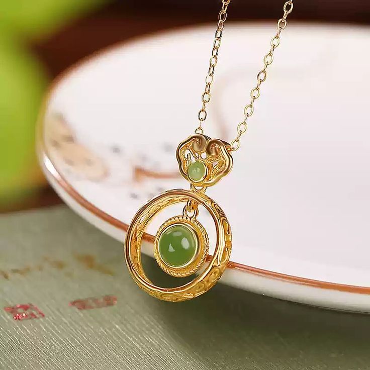 Material: S925 Sterling Silver with Gold PlatingGemstone: Jade, approximately 5mm (large), 2mm (small)Weight: Approximately 1.5gSize: Pendant Length: 22mm, Width: 15mm Description:Embrace timeless elegance with this Jade Double Circle Pendant Necklace. The design features a larger jade gemstone encased in a delicately twisted gold-plated S925 sterling silver frame, complemented by a smaller jade accent at the top. The double-circle structure offers a unique aesthetic that merges modern minimalism with traditional charm. This lightweight necklace is perfect for everyday wear, adding a refined touch to any outfit. The green jade's natural luster provides a subtle yet captivating appeal, making this piece an essential addition to your jewelry collection. Note: As jade is a natural gemstone, s Elegant Jade Necklace Round Shape, Elegant Jade Round Necklace, Elegant Round Jade Necklace, Elegant Jade Necklaces As Gifts, Elegant Jade Necklace For Gifting, Elegant Jade Necklaces For Gifts, Elegant Jade Necklace As Gift, Elegant Jade Necklace, Elegant Jewelry With Round Pendant And Natural Stones