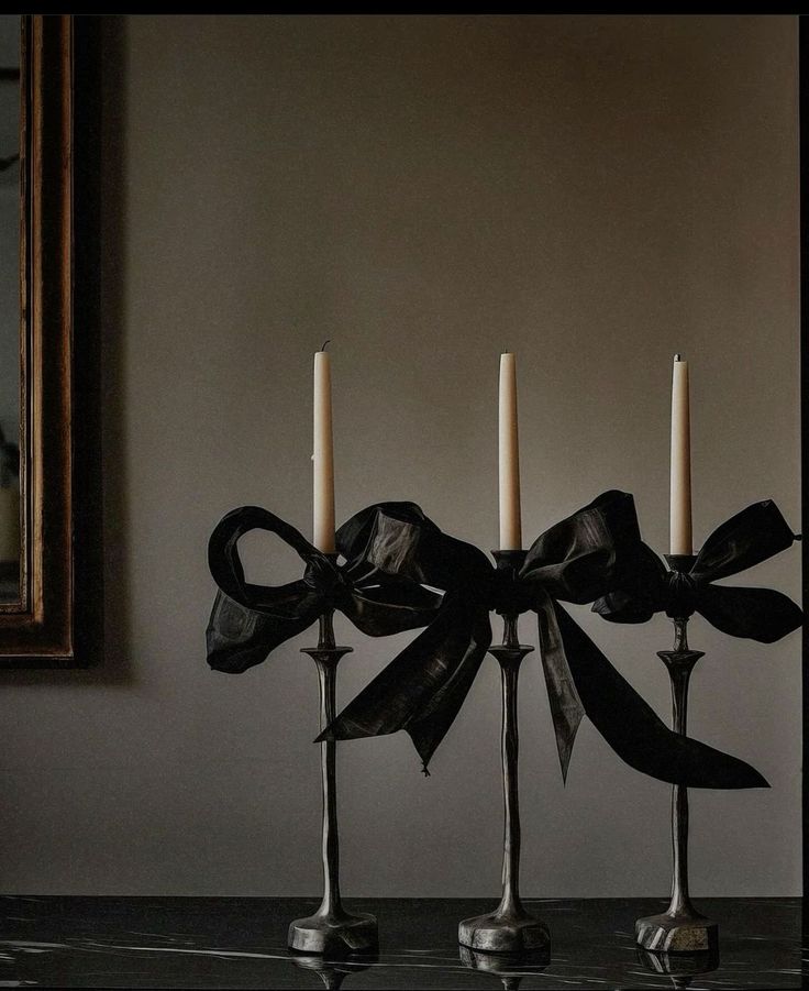 three candles with black bows on them are sitting in front of a painting and mirror