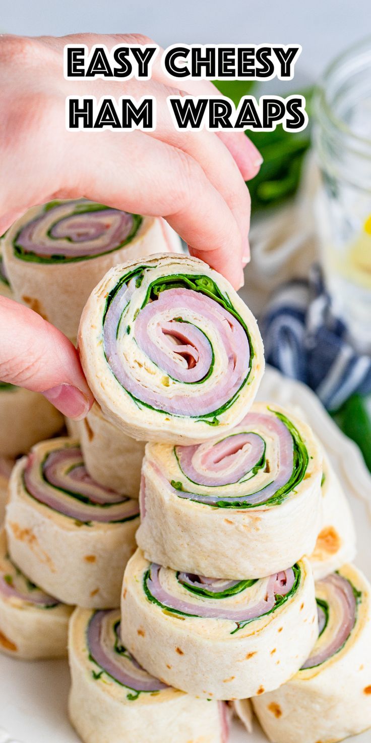 a hand is grabbing some ham wraps from a white plate