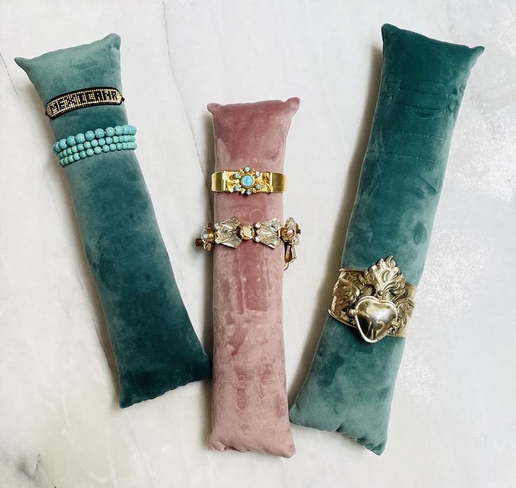 three different colored pillows with gold rings and beads on them, one is pink and the other is green