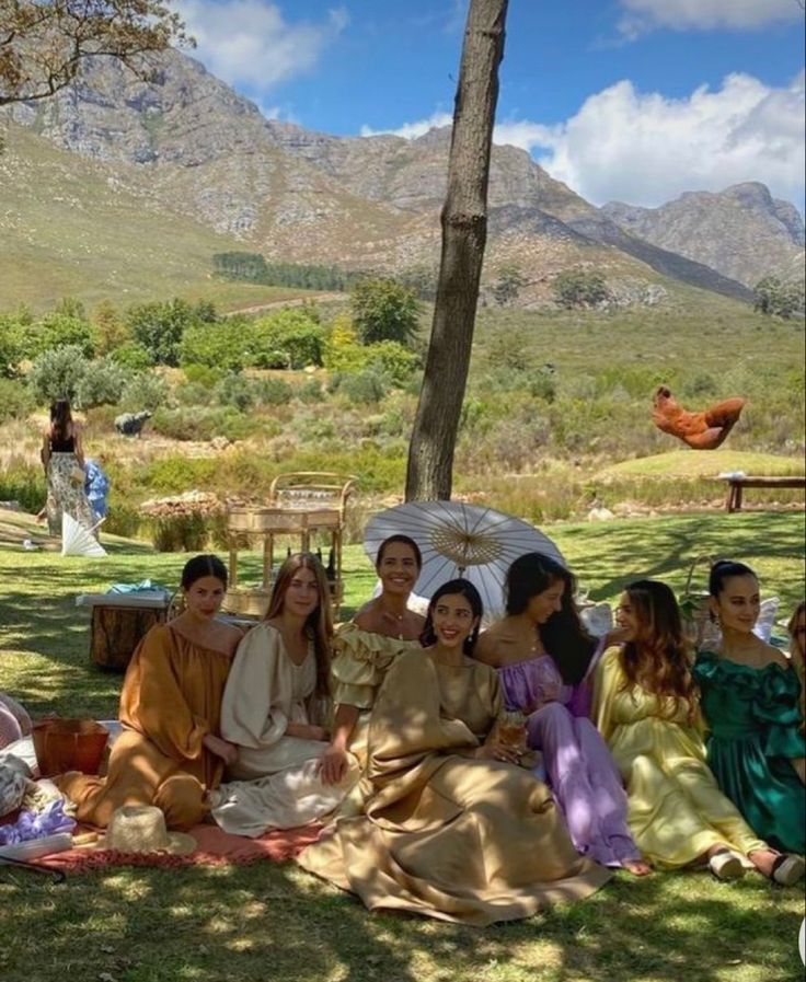 a group of women sitting on top of a blanket under a tree