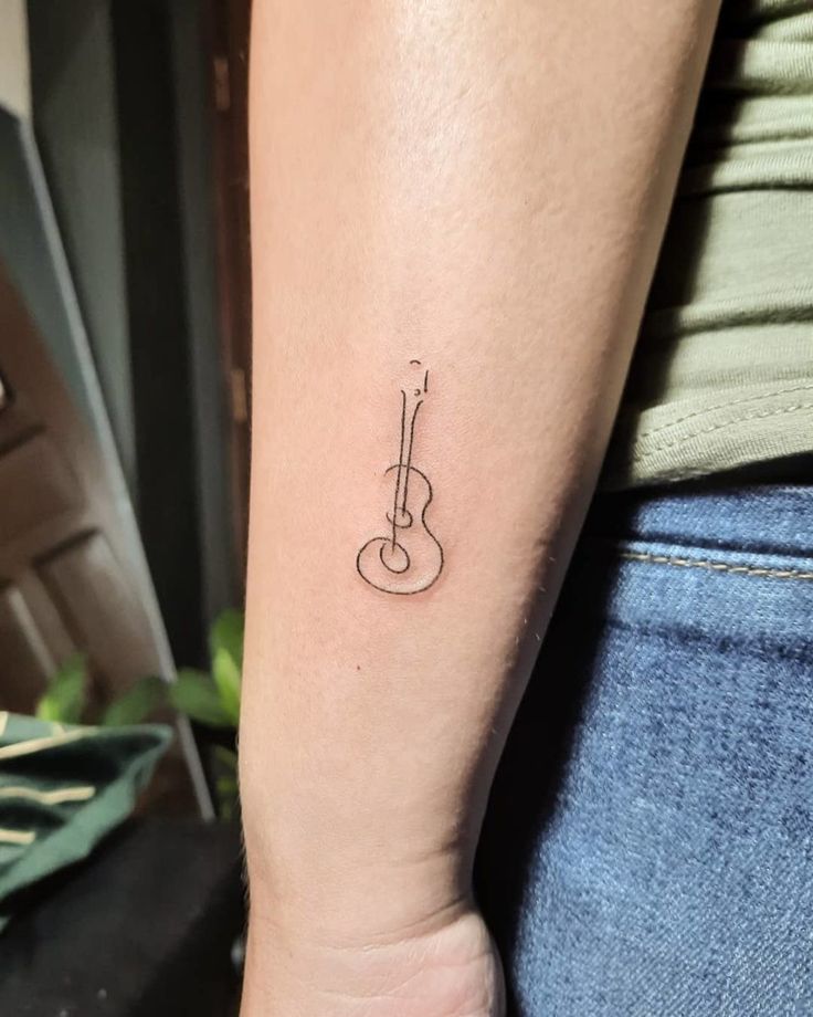 a small tattoo on the arm of a woman with a guitar in front of her