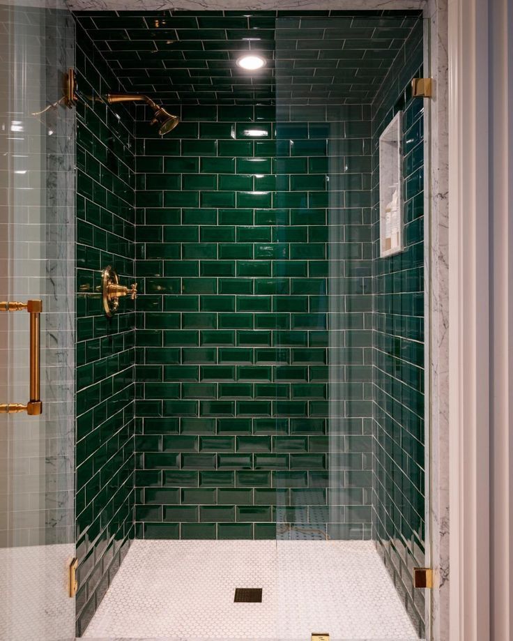 a green tiled shower with gold fixtures and white tile flooring in a small bathroom