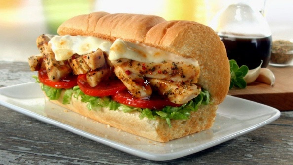 a chicken sandwich with tomatoes and lettuce on a white plate