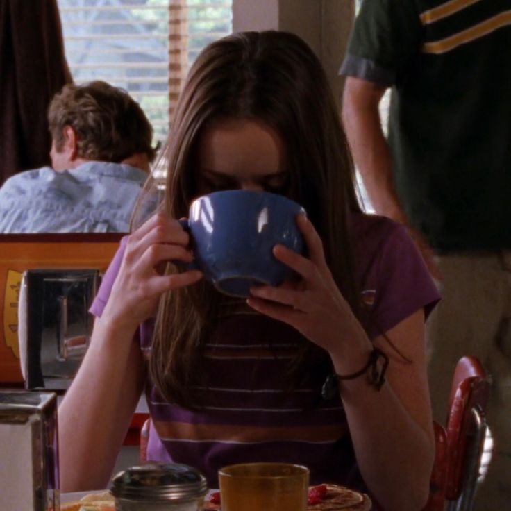 a woman sitting at a table drinking from a cup