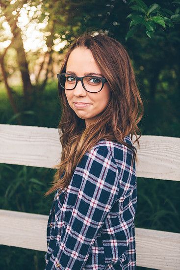 a woman wearing glasses standing in front of a fence with her hands on her hips