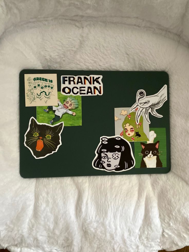 a green tray with stickers on it sitting on a white blanket next to a black and white cat