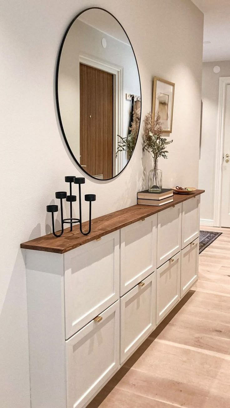 a large mirror on the wall above a long white cabinet with drawers and hooks in front of it