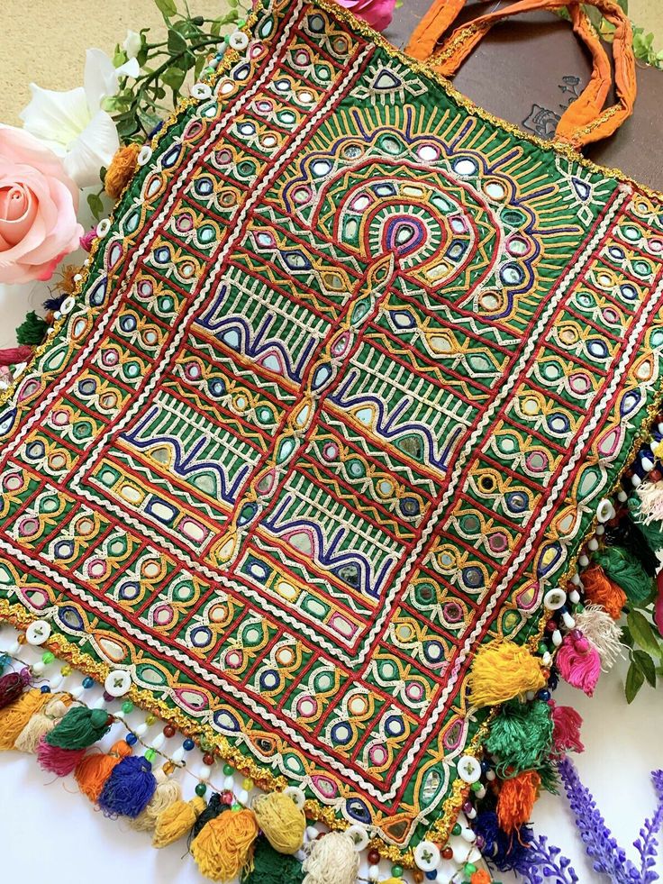 an embroidered bag sitting on top of a table next to flowers and a purse with tassels hanging from it