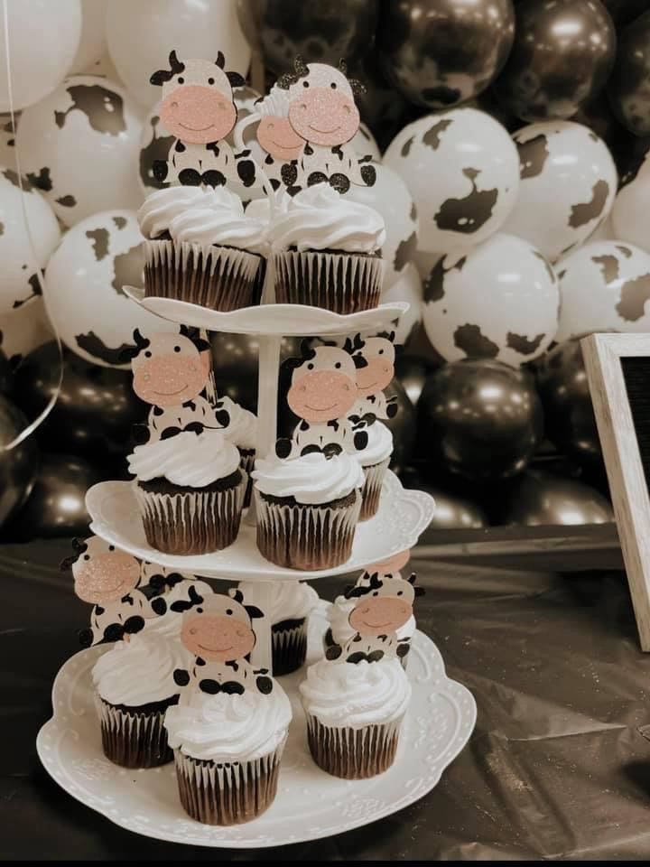 cupcakes are stacked on top of each other in front of balloons and cow decorations