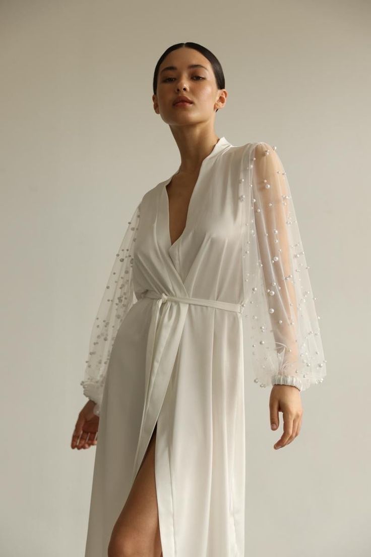 Our long bridal silk robe with wide long sheer sleeves with pearls. The robe is both casual and elegant, you may wear it on the hen party or spontaneously around your home on a daily basis. It is also an amazing outfit for your vocation, to wear it on the beautiful beach or by the pool as a cover up. Model is 168 cm, 84/64/89 wears size XS  Total length 135 cm  Off white color Elegant V-neck Kimono For Wedding, Elegant V-neck Wedding Kimono, Sheer Long Sleeve Robe For Wedding Night, Elegant Long Sleeve Nightgown, Elegant Evening Nightgown For Spring, Elegant Open Front Kimono For Wedding, Elegant Sheer Party Kimono, Feminine Wedding Robe With Kimono Sleeves, Sheer Long Sleeve Wedding Nightgown