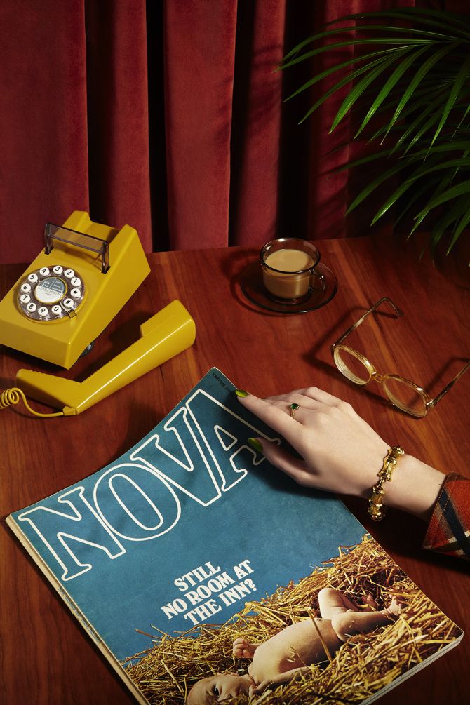 a woman's hand on top of a magazine next to a phone and eyeglasses