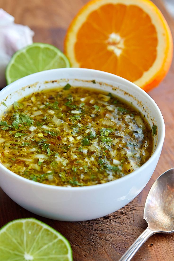 a white bowl filled with green sauce next to sliced oranges and lime wedges