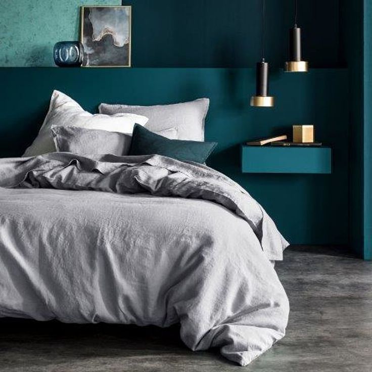 a bed with grey linens and pillows in a room painted teal green, white and gold