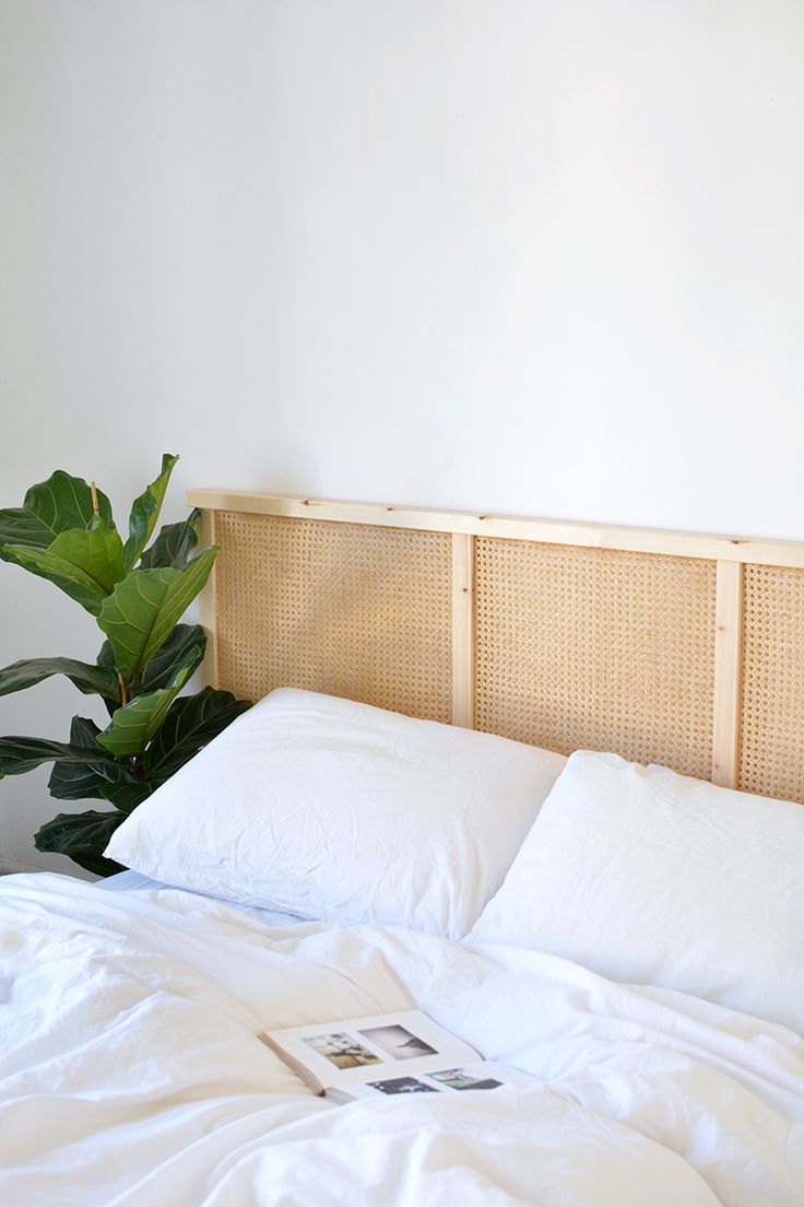 a bed with white sheets and pillows next to a plant