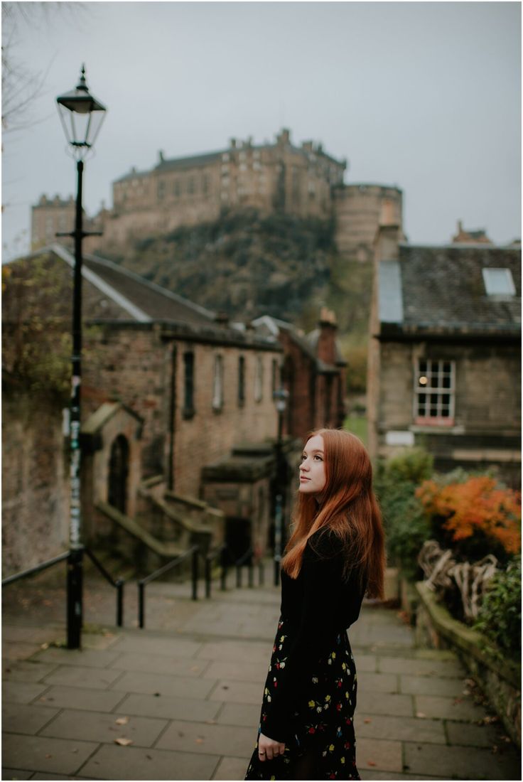 a woman with red hair standing in front of a castle