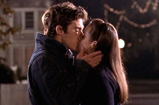 a man and woman kissing each other in front of a house with christmas lights behind them