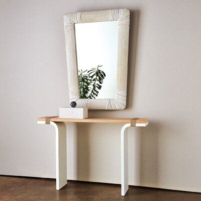 a mirror sitting on top of a wooden table next to a white vase with a plant in it