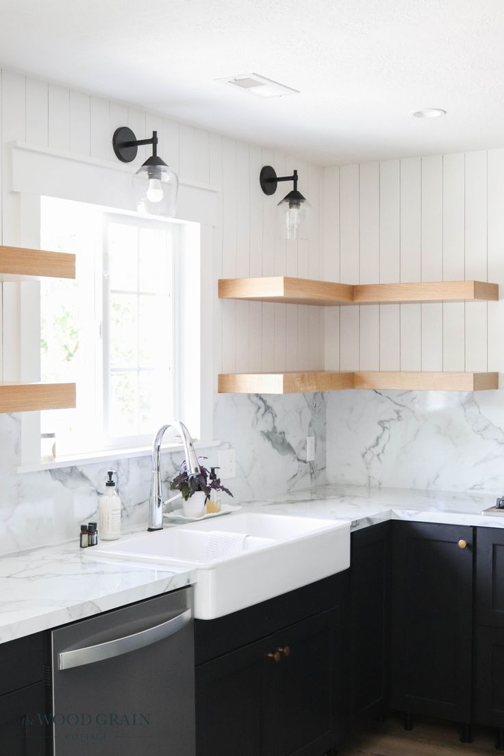 a kitchen with black cabinets and white marble counter tops, wooden shelves above the sink