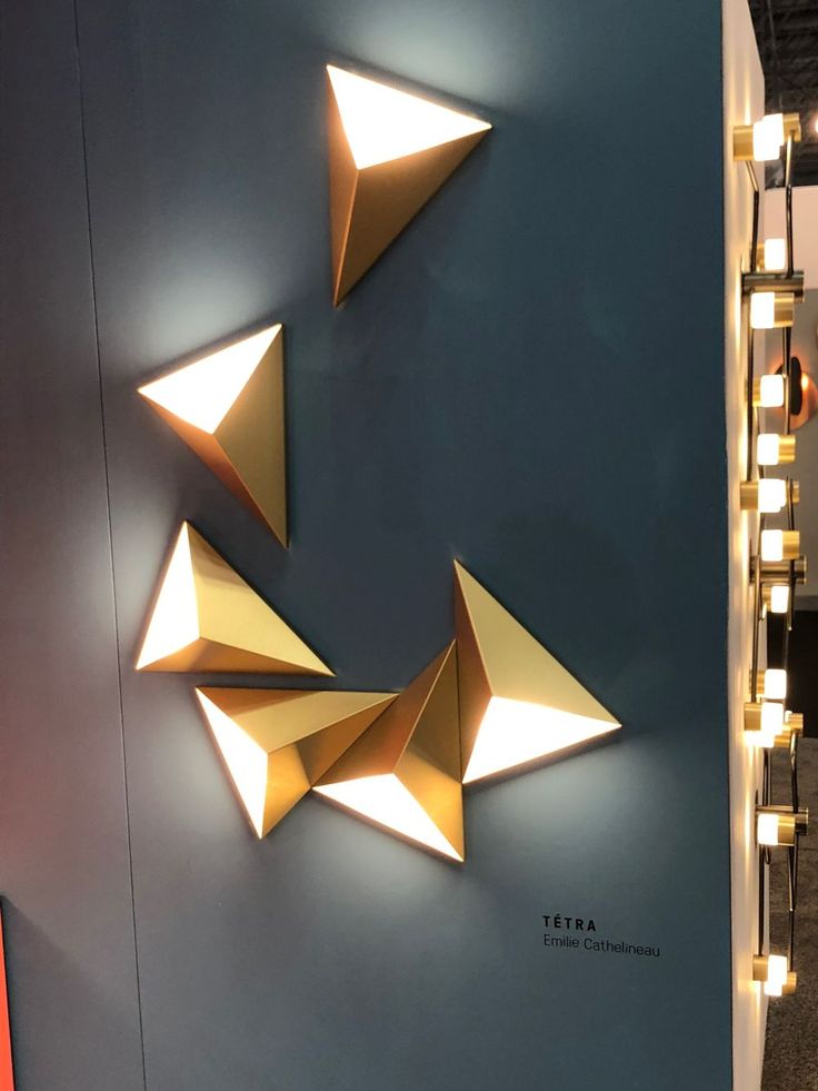 three gold origami shapes on a blue wall with lights around the edges and below them