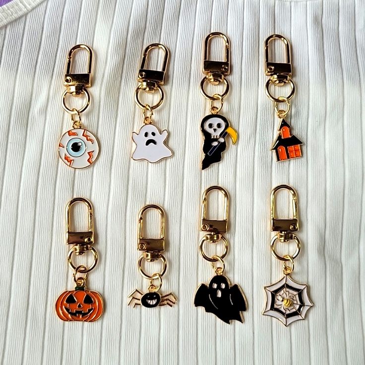 six halloween themed keychains on a white fabric background, one has a ghost, the other is a jack - o'- lantern