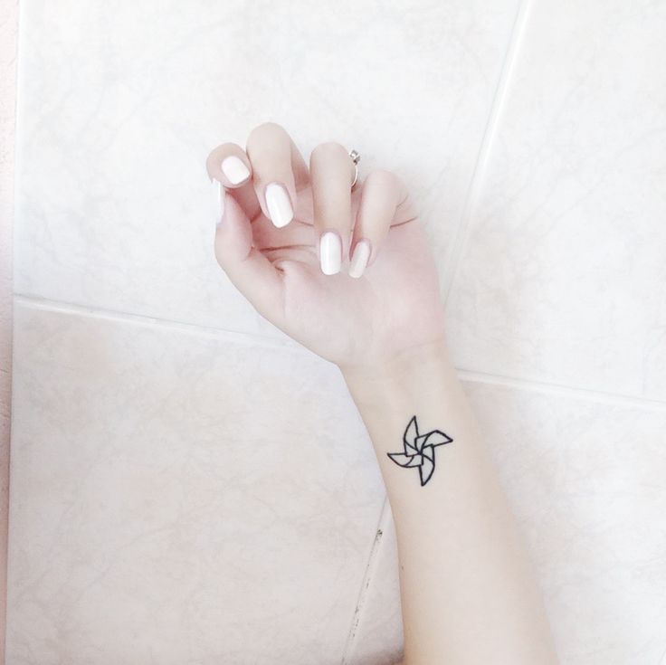 a woman's hand with a small tattoo on her left wrist, resting against a white tile wall