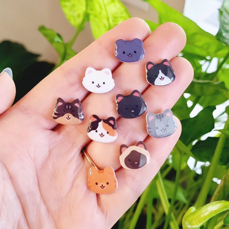 a person holding six small animal pins in their hand with plants in the back ground