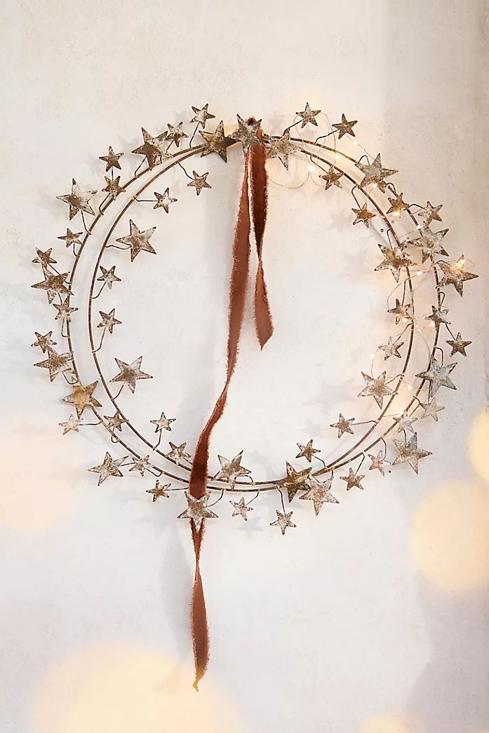 a metal wreath with stars hanging from it's side on a white wall next to string lights