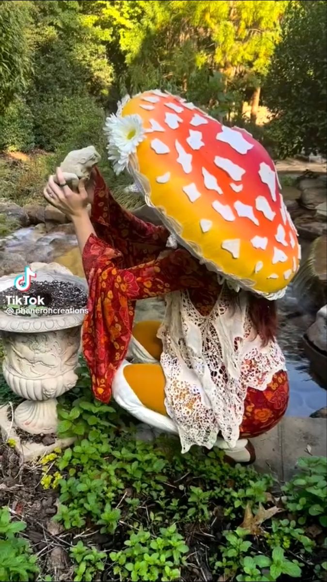 a woman kneeling down next to a large mushroom on top of a stone planter