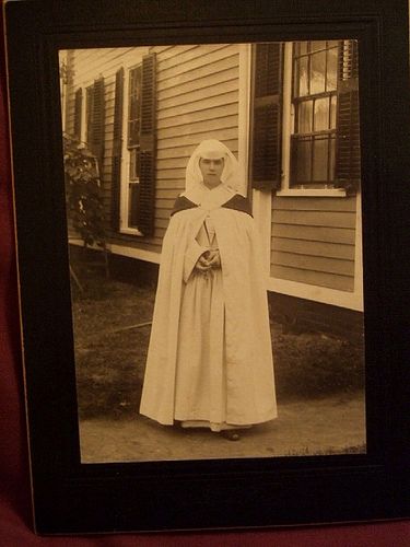 an old black and white photo of a nun standing in front of a house