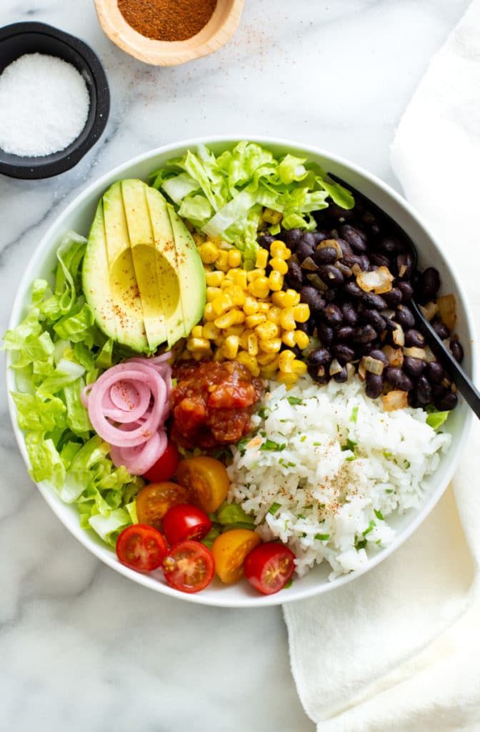 a white bowl filled with rice, beans, avocado and other veggies