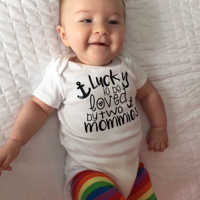 a baby laying on top of a bed wearing a shirt that says lucky to be loved by two mommas