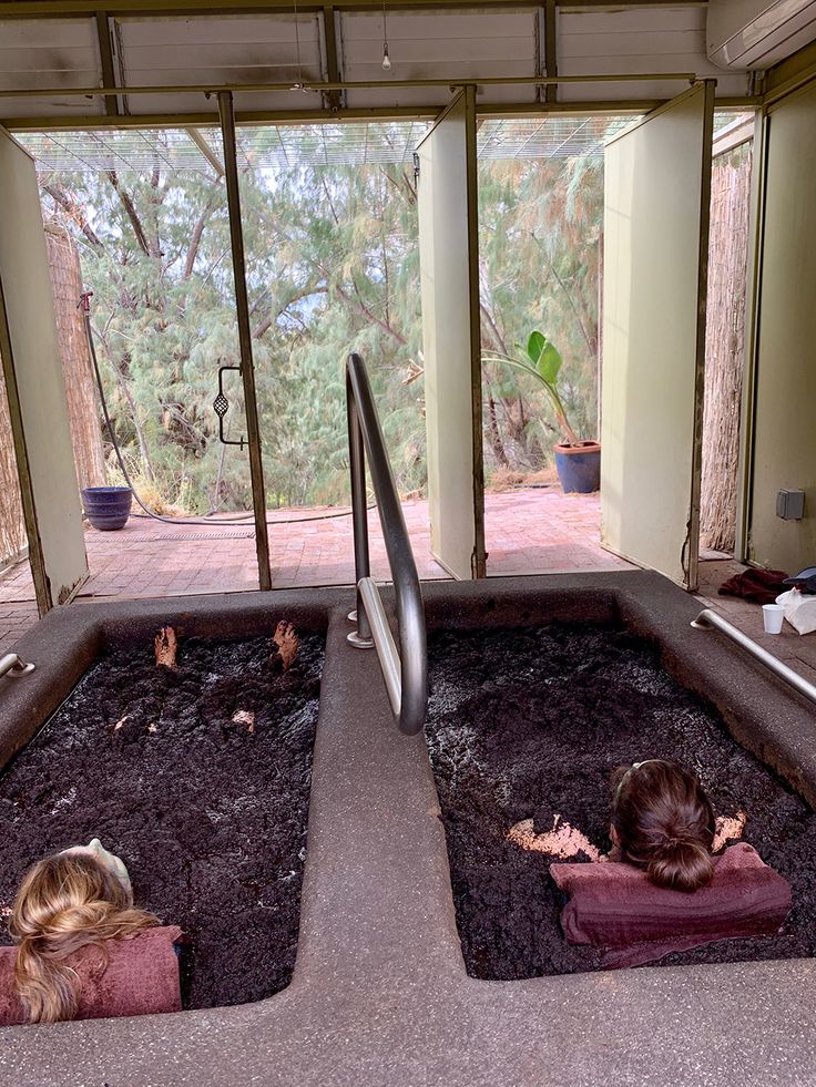 two children are sitting in the middle of an indoor swimming pool with dirt on the ground