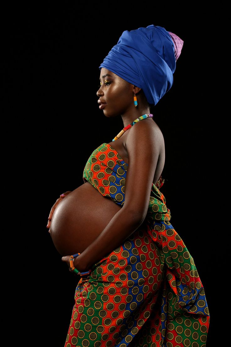 a pregnant woman in a colorful dress and head scarf is standing with her hands on her belly