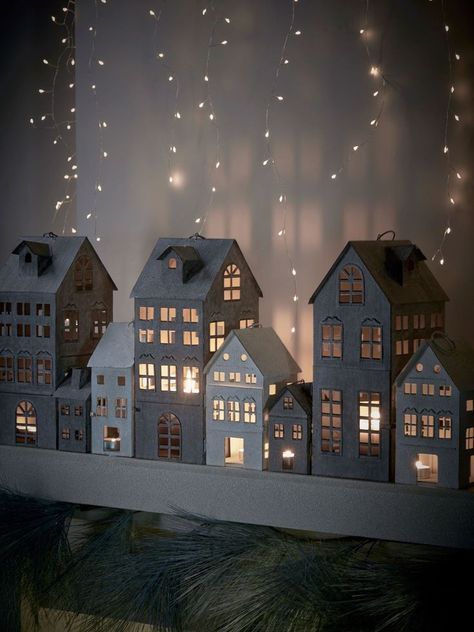 a group of miniature houses sitting on top of a table next to a window covered in string lights