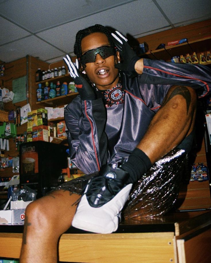 a man sitting on top of a wooden table wearing black and silver clothing with his hands in his hair