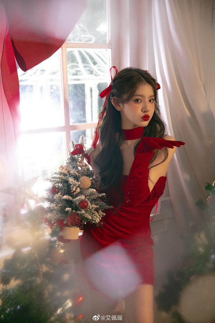 a woman in a red dress standing next to a christmas tree with her hands on her hips