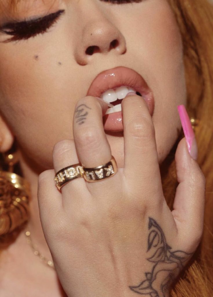 a close up of a person with tattoos on her face and hands holding a ring