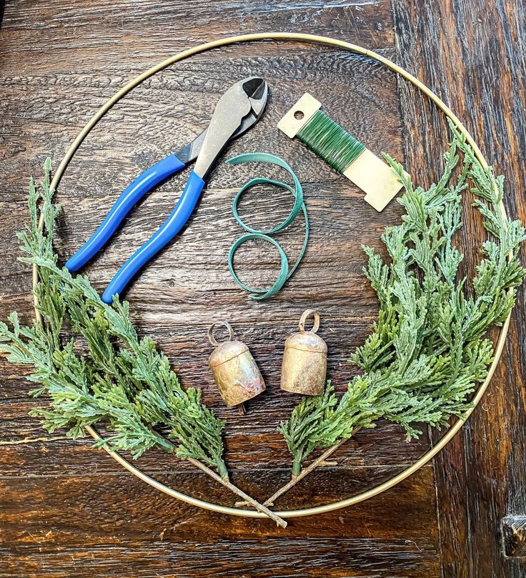 a wooden table topped with scissors and other items on top of a circle covered in greenery