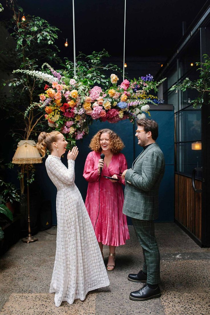 a man and woman standing in front of a flower arch with flowers hanging from the ceiling