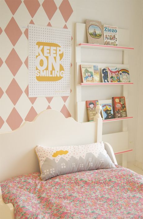 a child's bedroom with pink and white wallpaper, bookshelves and bed