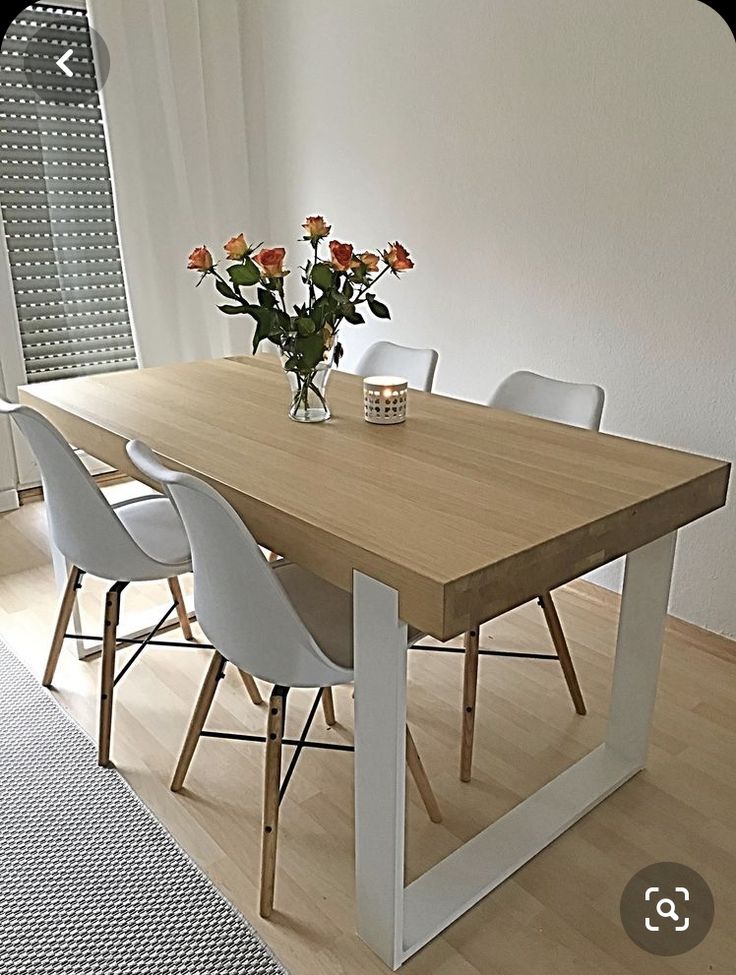 a wooden table with white chairs and flowers in vase on the top, next to a window