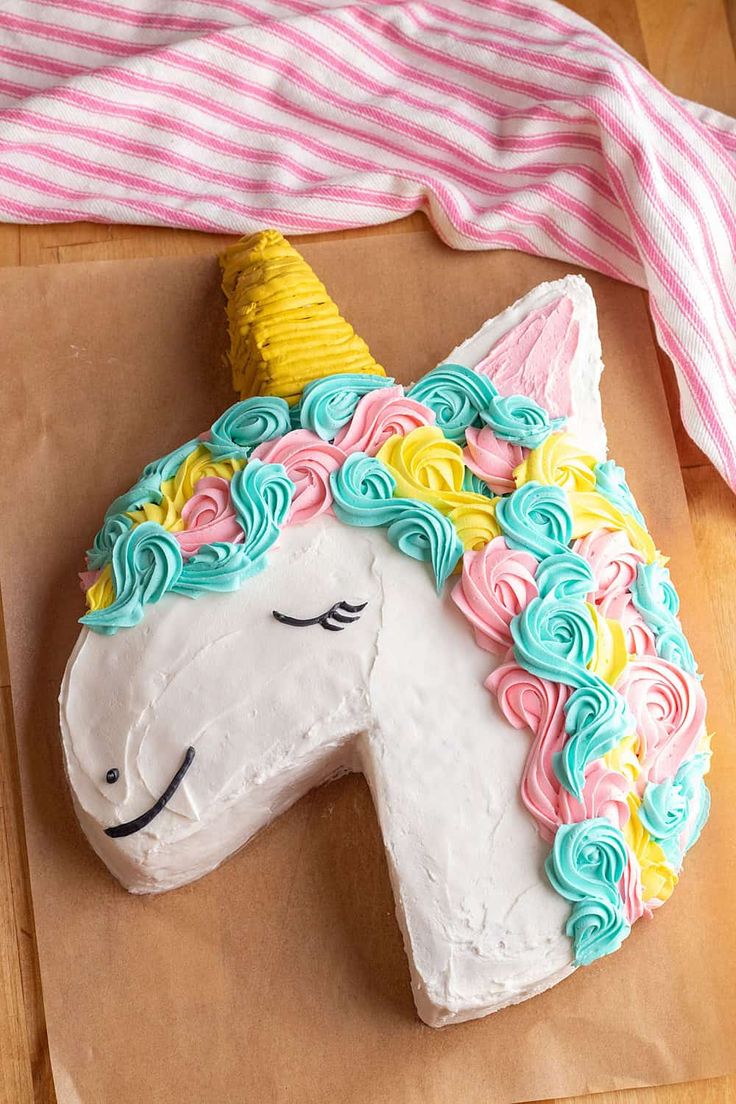 a cake shaped like a unicorn on top of a piece of brown paper next to a pink and white striped towel