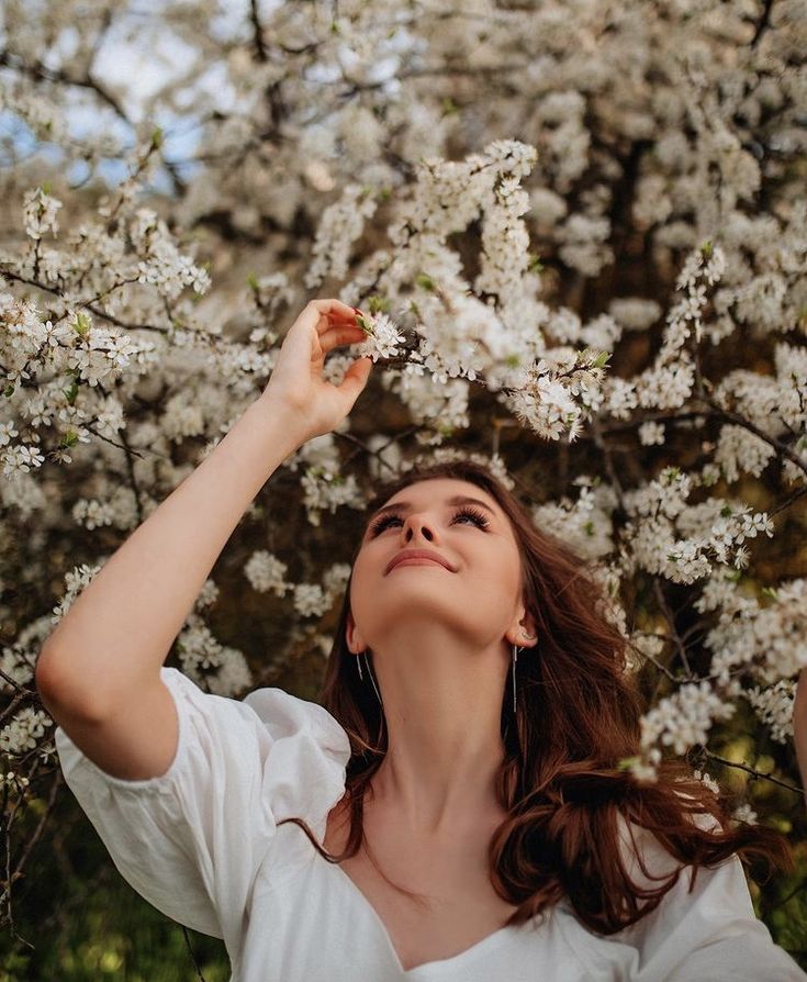 a woman standing in front of a tree with white flowers