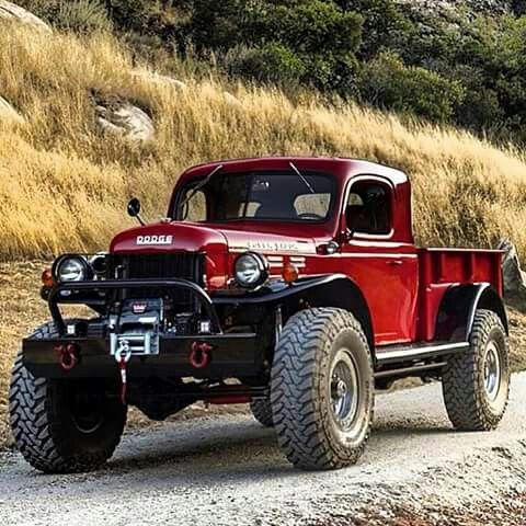 an old red pickup truck driving down a dirt road