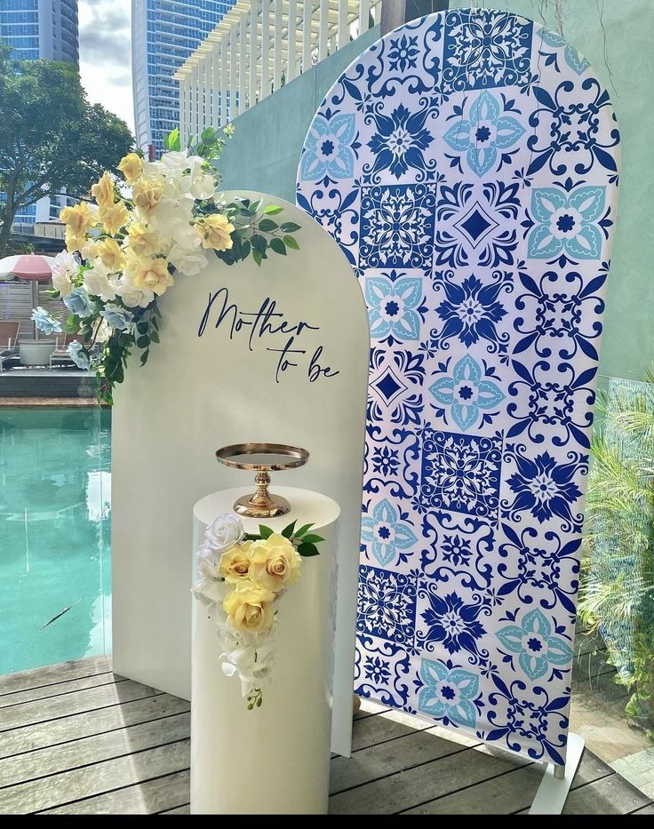 a water fountain with flowers on it next to a blue and white tile wall near a pool