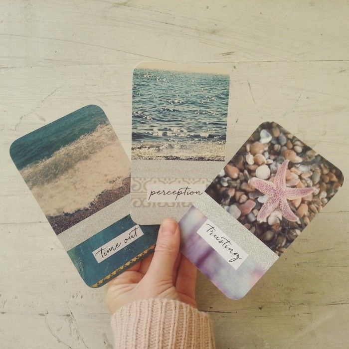 a person holding some cards with pictures on them and sand in front of the ocean