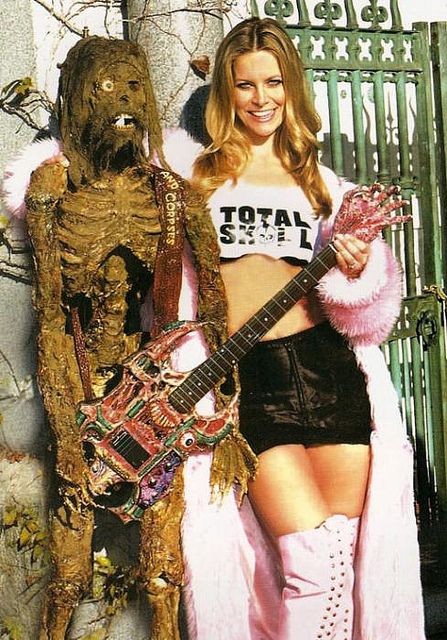 a woman standing next to a man dressed as a monster and holding an electric guitar