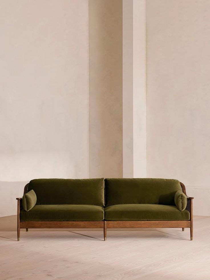 a green couch sitting on top of a wooden floor next to a white wall in an empty room