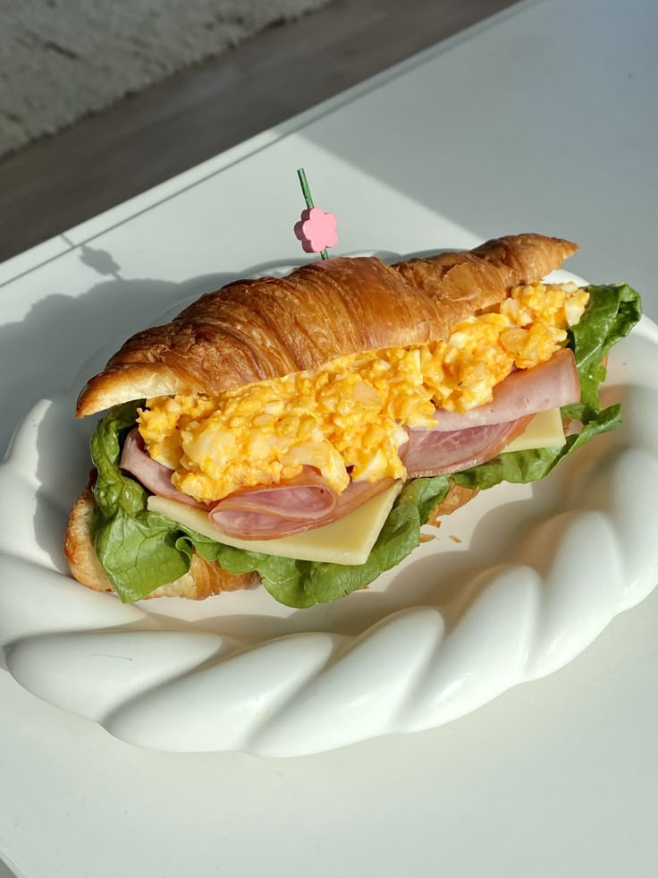 a sandwich with ham, cheese and lettuce sitting on a white paper plate